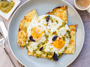Pesto fried eggs with Lo-Dough cheese toast on a grey plate with a coffee and cutlery 
