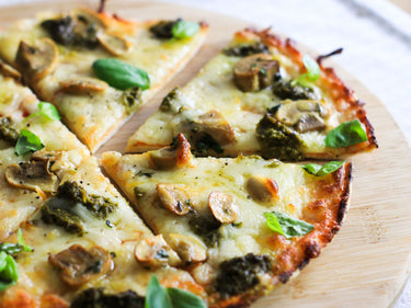 Healthy Lo-Dough pizza with mushrooms and pesto on a wooden chopping board